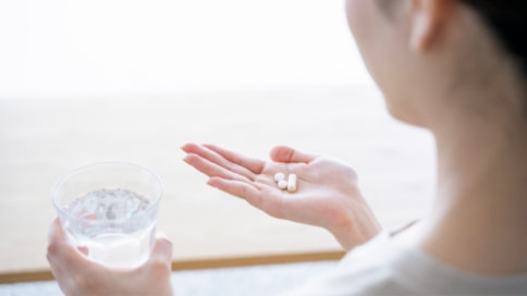 イメージ写真:錠剤と水の入ったグラスを手に持つ女性